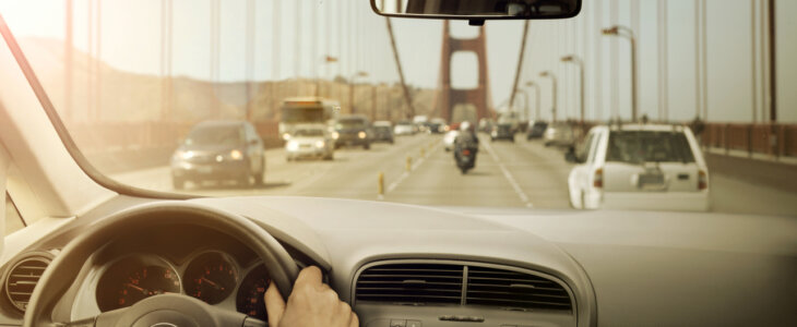 View from inside a car driving across the Golden Gate Bridge, showing the steering wheel, dashboard, and traffic ahead.
