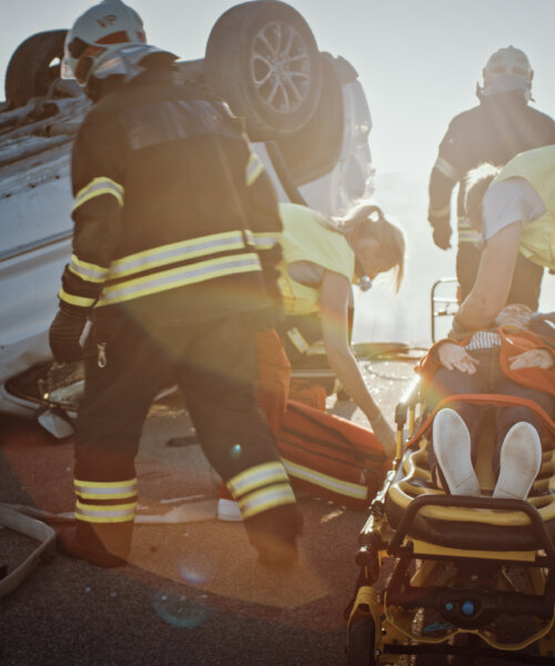 On the Car Crash Traffic Accident Scene: Rescue Team of Firefighters Pull Female Victim out of Rollover Vehicle, They Use Stretchers Carefully, Hand Her Over to Paramedics who Perform First Aid