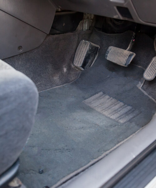 Gray cloth car mat in the interior of a Japanese sedan with three pedals gas, brake and clutch in a car service after dry cleaning.