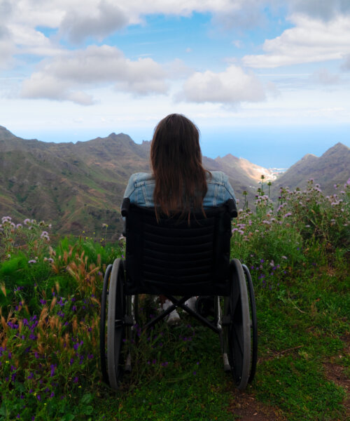 Rear view of young handicapped woman sitting on wheelchair on top of mountain
