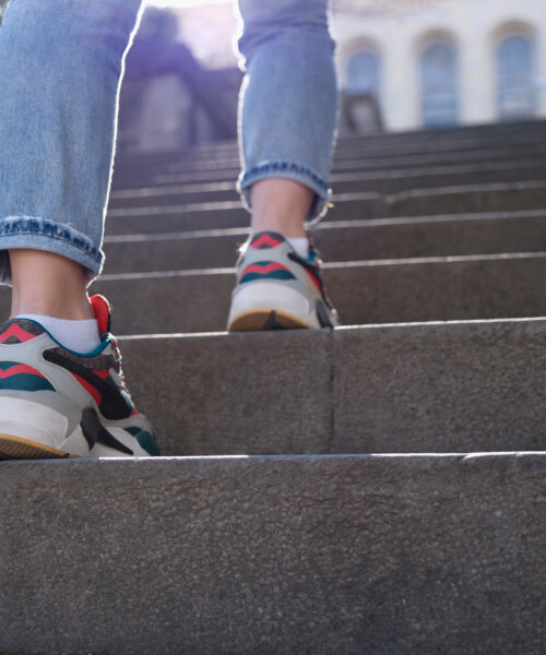 Female legs in sports sneakers going up stairs closeup. Hiking in city concept
