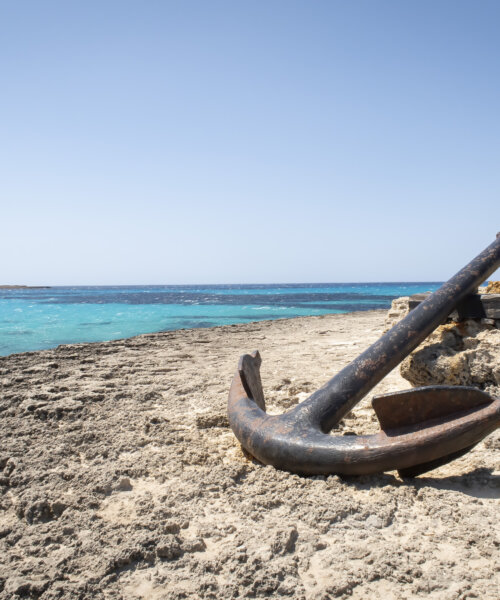 a large old anchor, stranded on a rocky cliff with a sea of turquoise water, copy space anchor of Punta Prima, Menorca, Spain