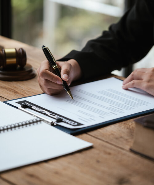 Close up of business's hand signing on agreement paperwork for selling and loan financial house properties.