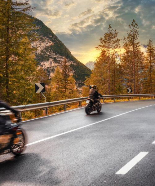 Travel concept. Group of people travelers on motorcycles ride on an asphalt road in the mountains at sunset in the Italian Alps. Beautiful autumn landscape
