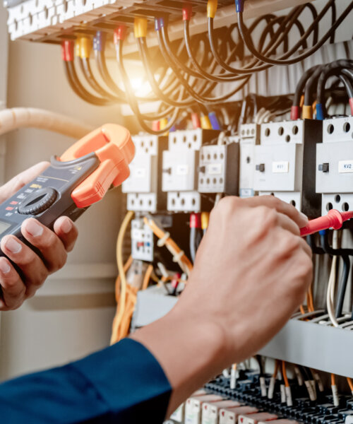 Electrician engineer uses a multimeter to test the electrical installation and power line current in an electrical system control cabinet.