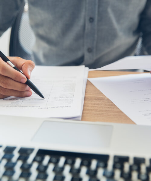 Unrecognizable businessman sitting at table holding ballpoint pen and papers and checking documents in office