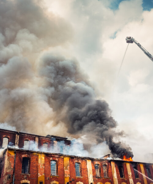 Firemen on the crane trying to extinguish a big fire. Grey clouds of smoke swirling out of an old abandoned building.