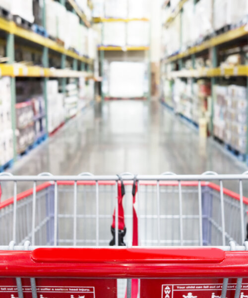 Interior warehouse super store with focus on empty shopping cart in store aisle.