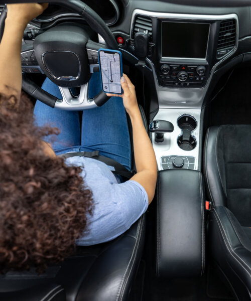 Latin American woman using the GPS on her cell phone while driving a car - navigation concepts