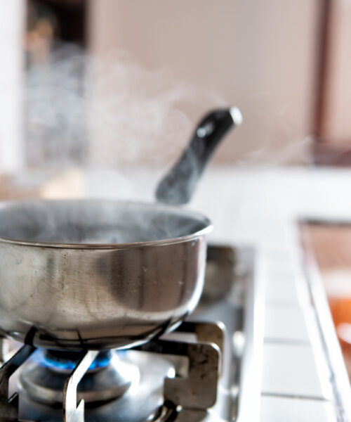 Closeup of vintage tiled gas stove top with tiles white countertop and stainless steel pot and steam cooking with blue flame in retro kitchen