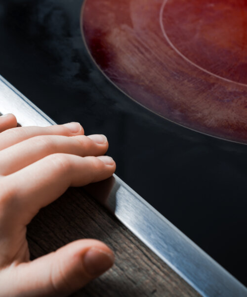 Hand Of A Child Reaches Active Hotplate Of Kitchen Glass-Ceramic Stove - Prevent Child Hazard Concept