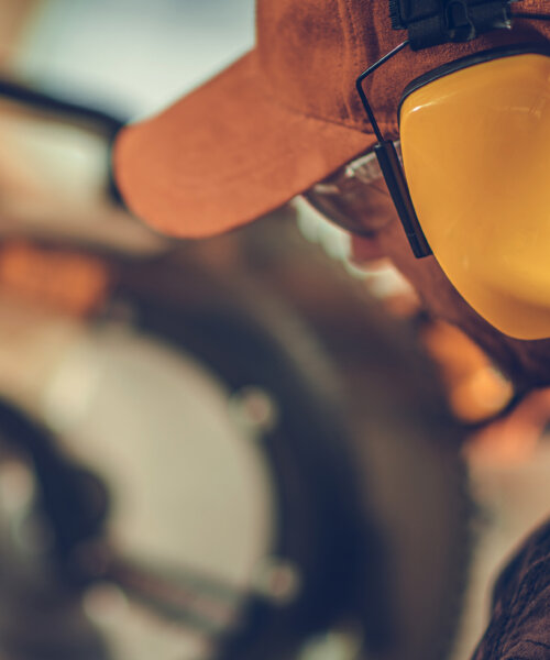 Caucasian Construction Worker in His 40s Wearing Noise Cancellation Safety Headphones While Working Within Construction Site.