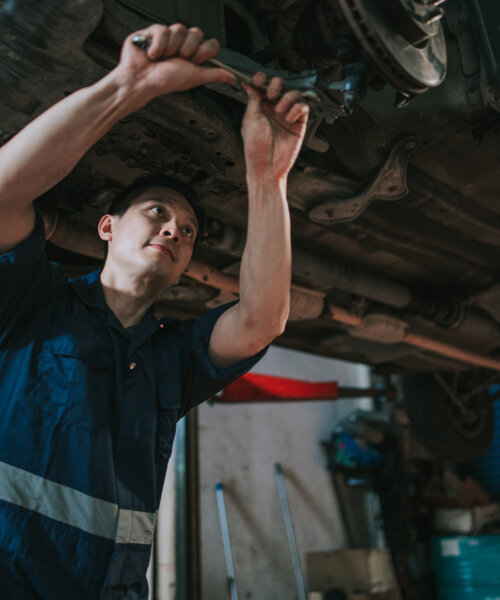 Asian Chinese mechanic checking car undercarriage in auto repair shop