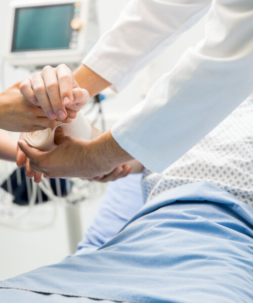 Closeup of the hands of two doctors bandaging a patient's arm in an emergency room