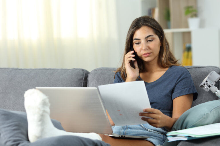 Woman with cast on leg sitting on the couch while on the phone looking at documents