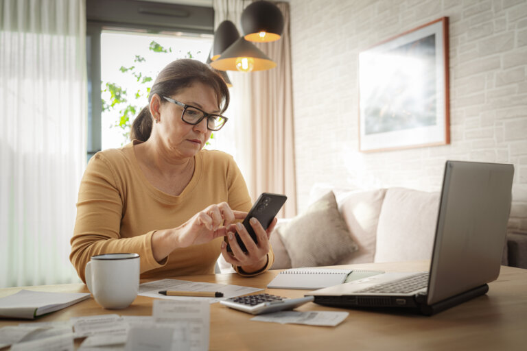 Woman using mobile phone and laptop working from home.