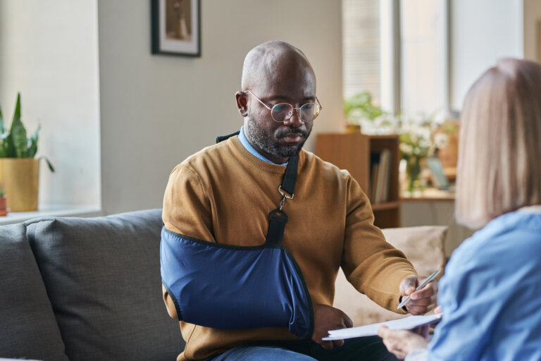 Portrait of adult African American man with broken arm signing contract for at home medical services on clipboard copy space
