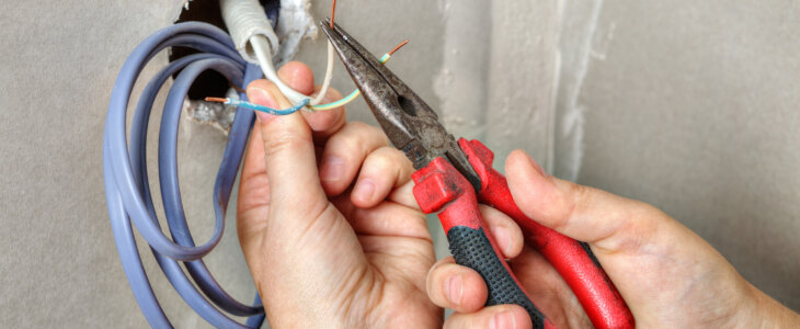 The electrician's hands stretch the wiring through the hole in the wall