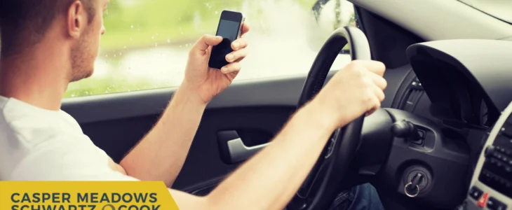 A driver holding a phone while steering, representing the dangers of distracted driving.
