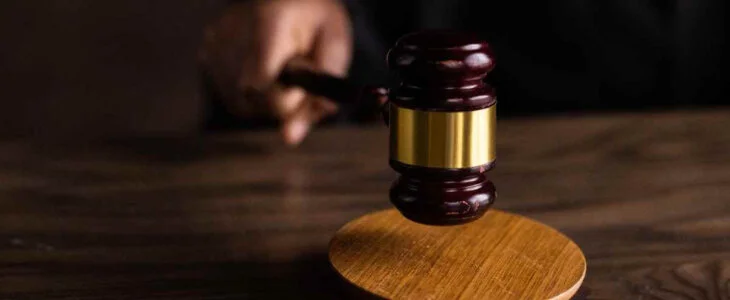 A judge's gavel being struck on a wooden block in a courtroom setting.