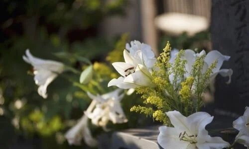 A bouquet of white lilies and yellow flowers placed on a grave marker.
