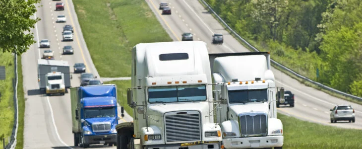 Semi-trucks and cars driving along a busy highway surrounded by greenery.