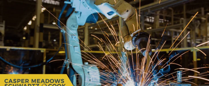 A robotic arm welding metal with bright sparks flying in a factory, featuring the logo of Casper Meadows Schwartz & Cook, Bay Area injury attorneys.