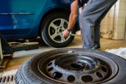 A mechanic is changing a tire on a blue car, using a wrench to loosen the bolts, with a spare tire on the ground nearby.