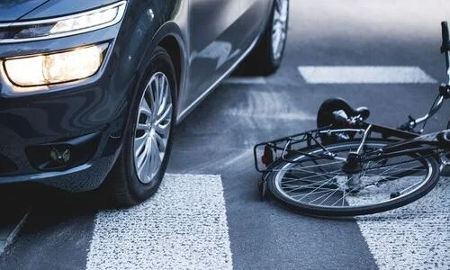 A car stopped at a crosswalk next to a fallen bicycle, suggesting a collision.