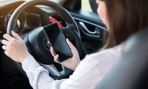 A woman driving while holding a smartphone, distracted from the road.