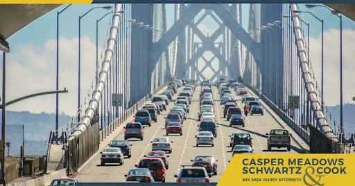 View of heavy traffic crossing the San Francisco Bay Bridge, with numerous vehicles on the lanes, and the logo of Casper Meadows Schwartz & Cook, Bay Area Injury Attorneys.