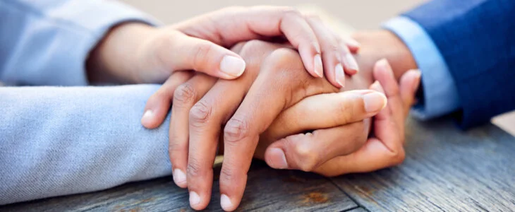 Two people holding each others hands in consolation