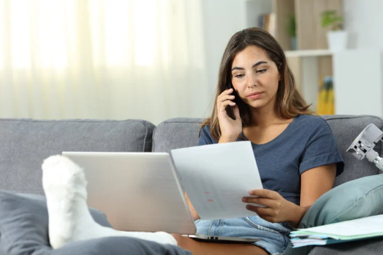Woman with cast on leg sitting on the couch while on the phone looking at documents