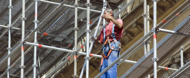 Construction worker on scaffolding wearing safety harness while assembling structure