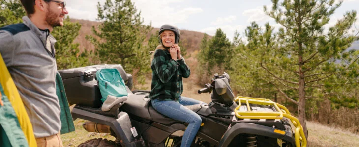 Woman sitting on an ATV fastening her helmet while man stands nearby outdoors