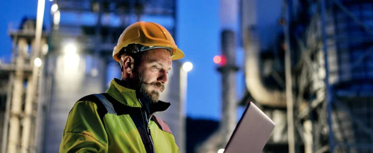 Young engineer wearing a helmet and using a laptop during his night shift.