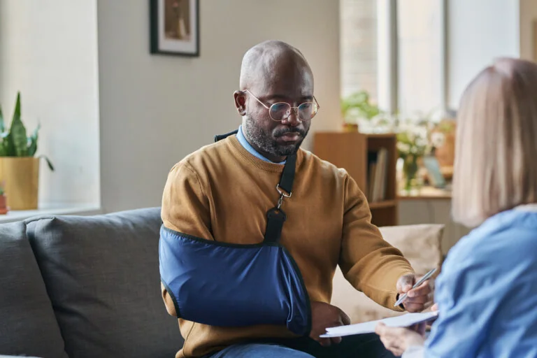 Portrait of adult African American man with broken arm signing contract for at home medical services on clipboard copy space